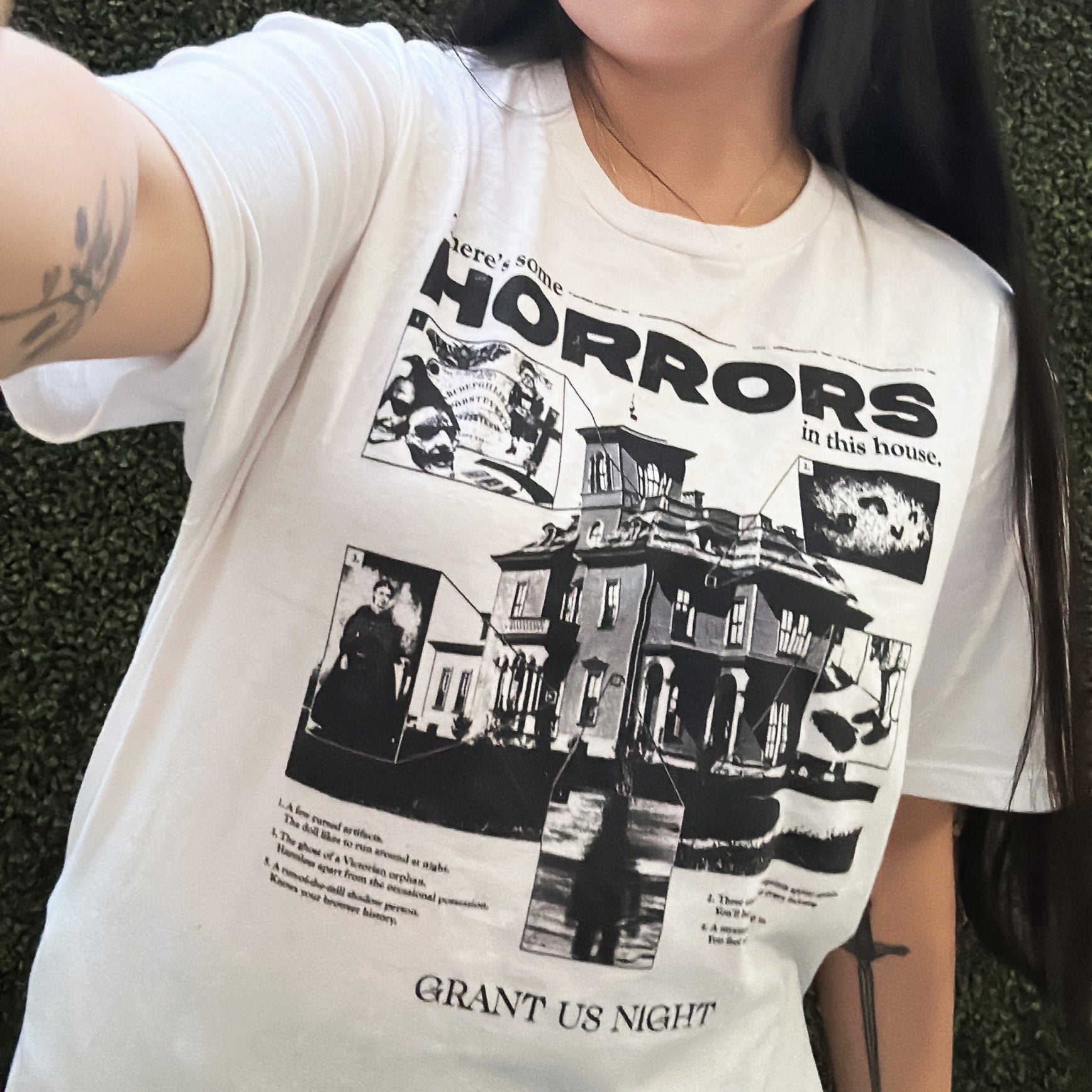 Person wearing Grant Us Night white Horror House T-shirt with black graphic design text and a haunted house with ghosts and footprints and cursed objects and illustrations on a textured background
