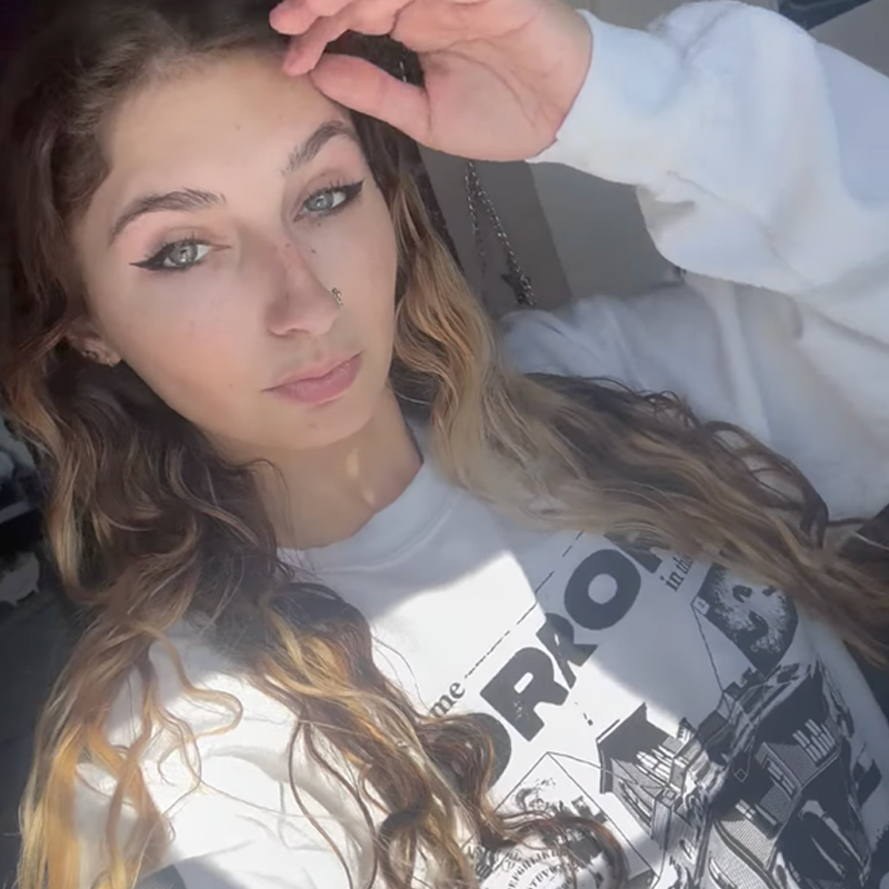 Person with long wavy hair wearing a white Grant Us Night sweatshirt with black text and graphics.