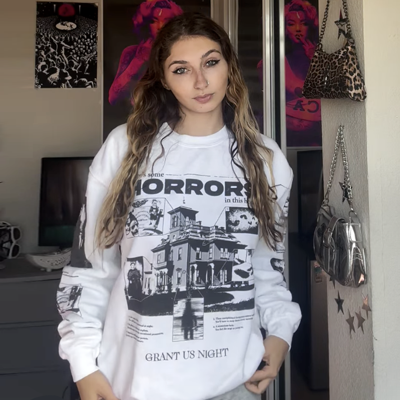 Person wearing a white Grant Us Night sweatshirt with black graphic design in a room.