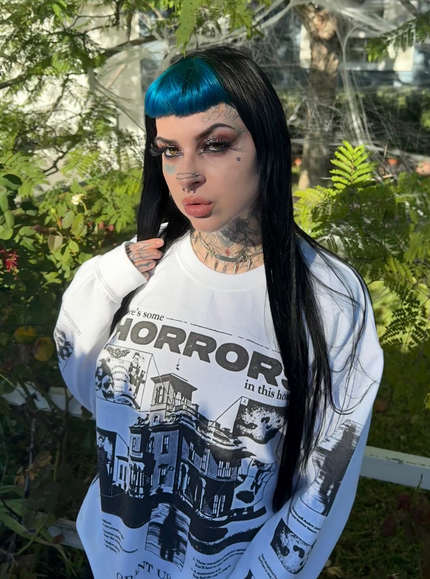 Person wearing a white Grant Us Night sweatshirt with black graphics and text, standing outdoors with greenery in the background.