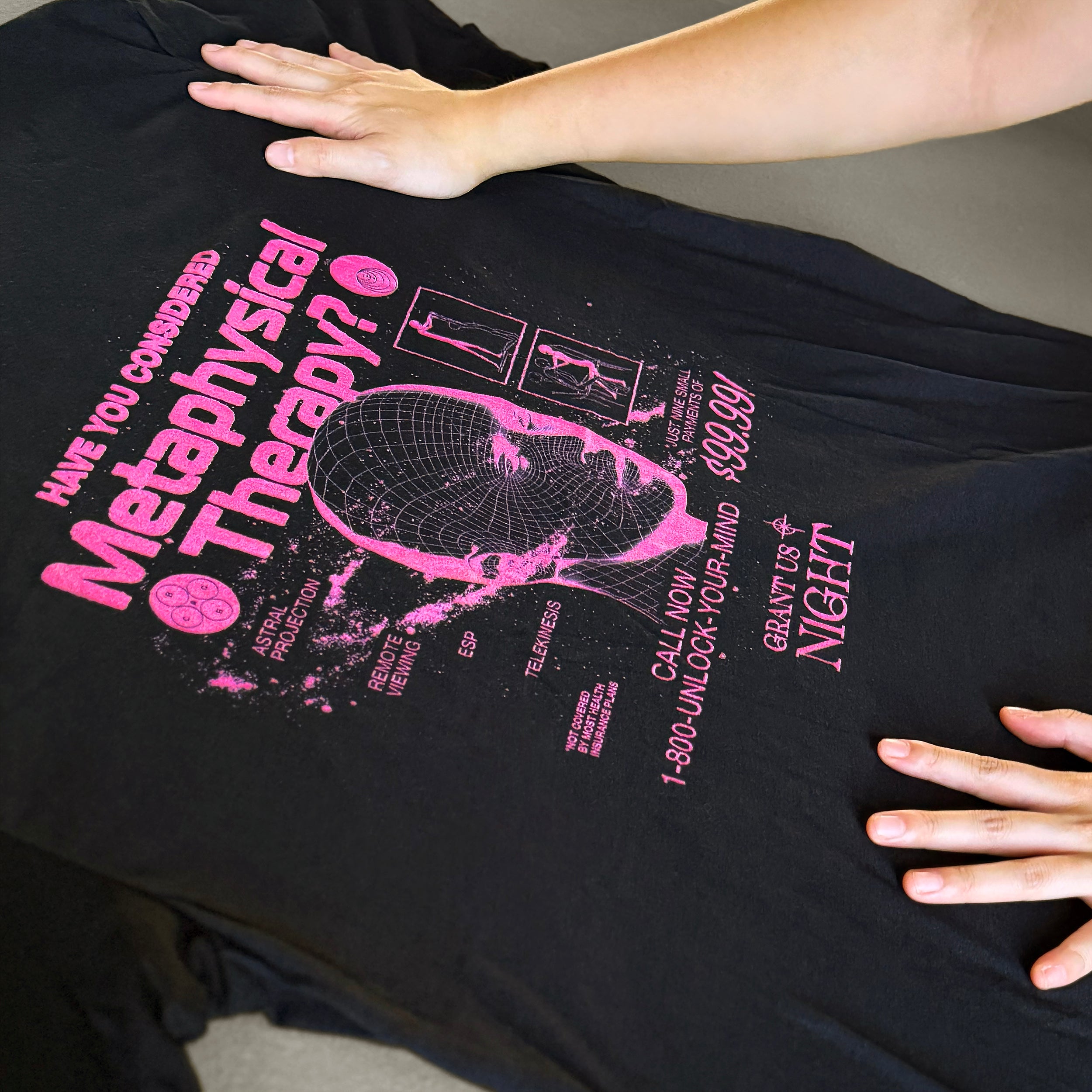Grant Us Night Metaphysical Therapy black shirt with pink purple fuschia text graphic design of a 3D mesh human head and a galaxy and alien diagrams held by a person