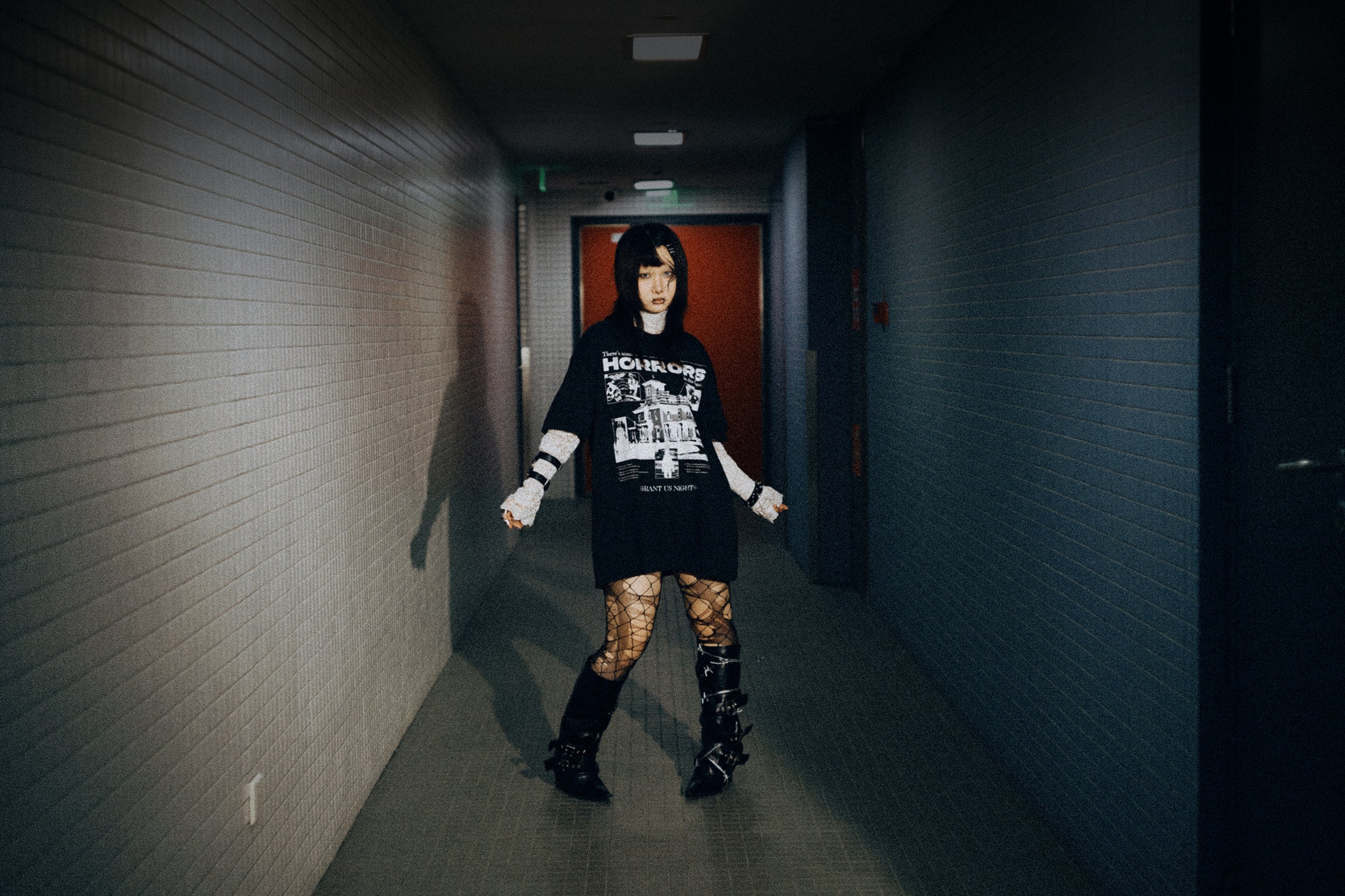 Person wearing a black outfit with white text in a dimly lit hallway